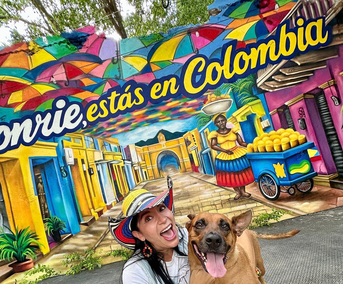 Mural de Parceros con la frase «Sonríe, estás en Colombia» sobre casas de colores y una chiva