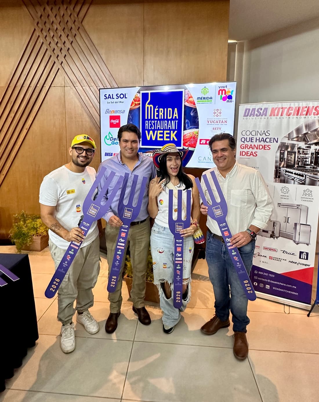El equipo de Parceros —gorra de Colombia, camiseta con la bandera y sombrero vueltiao— posando con dos autoridades del evento, los cuatro con tenedores gigantes del Mérida Restaurant Week