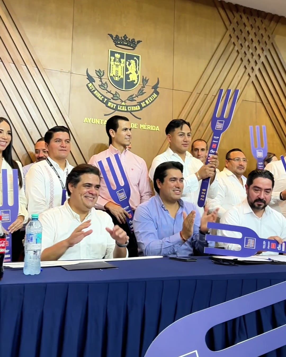 Presídium de la presentación del Mérida Restaurant Week en el Ayuntamiento de Mérida, bajo el escudo de la ciudad, con los asistentes sosteniendo los tenedores morados del evento.