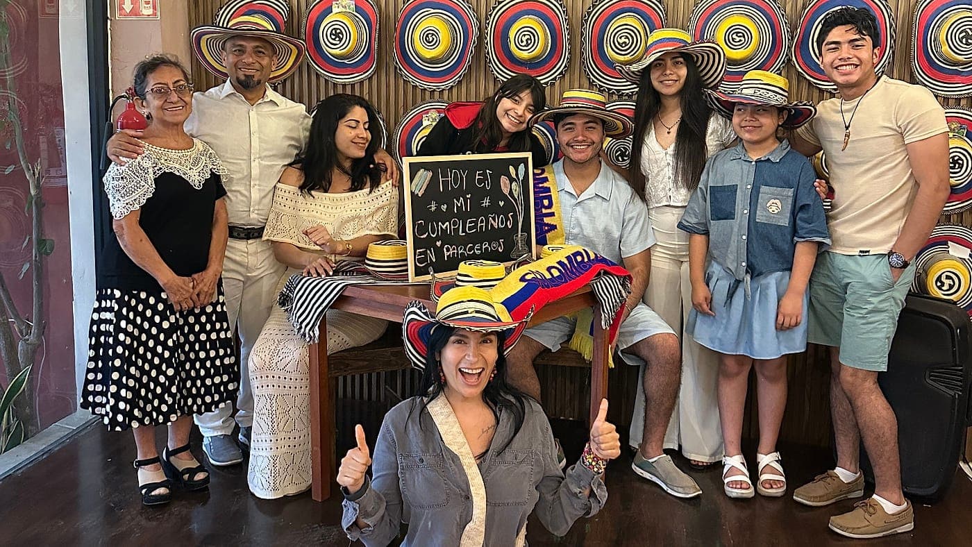 Una familia de nueve posando con sombreros vueltiaos ante la pared de sombreros de Parceros, con el pizarrón de «Hoy es mi cumpleaños en Parceros»