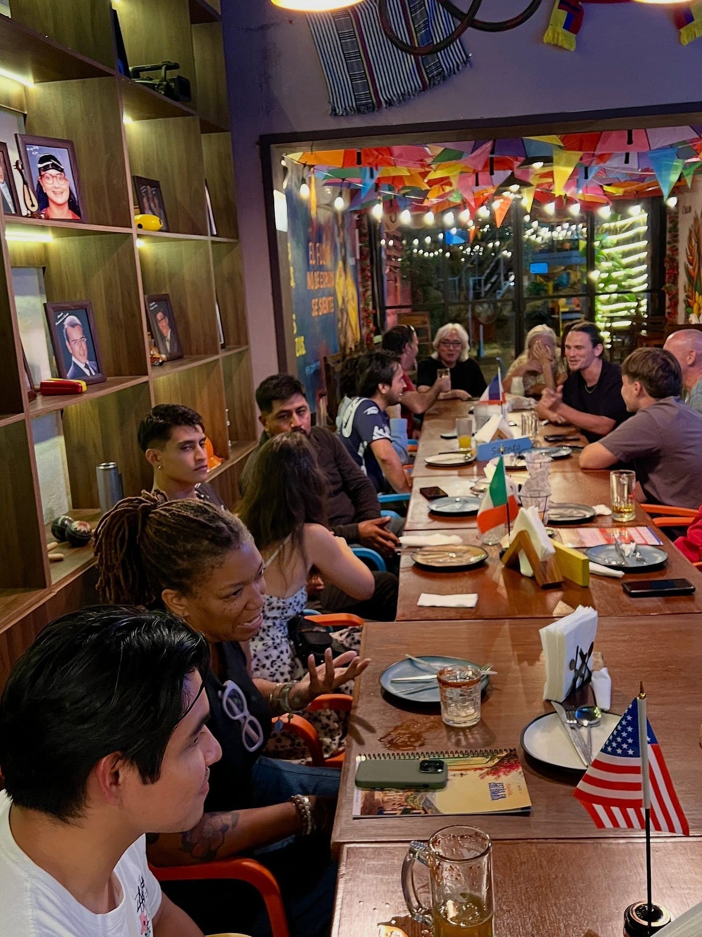 La mesa larga vista a lo largo, con banderitas de Francia, Irlanda y Estados Unidos repartidas entre los platos y gente hablando a ambos lados.