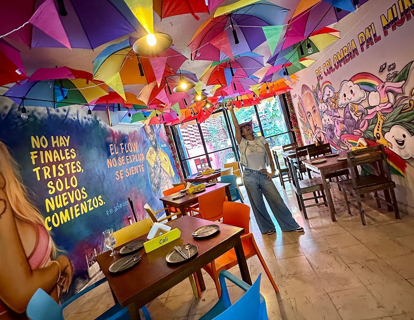 Interior de Parceros con el techo cubierto de sombrillas de colores, murales colombianos y mesas puestas