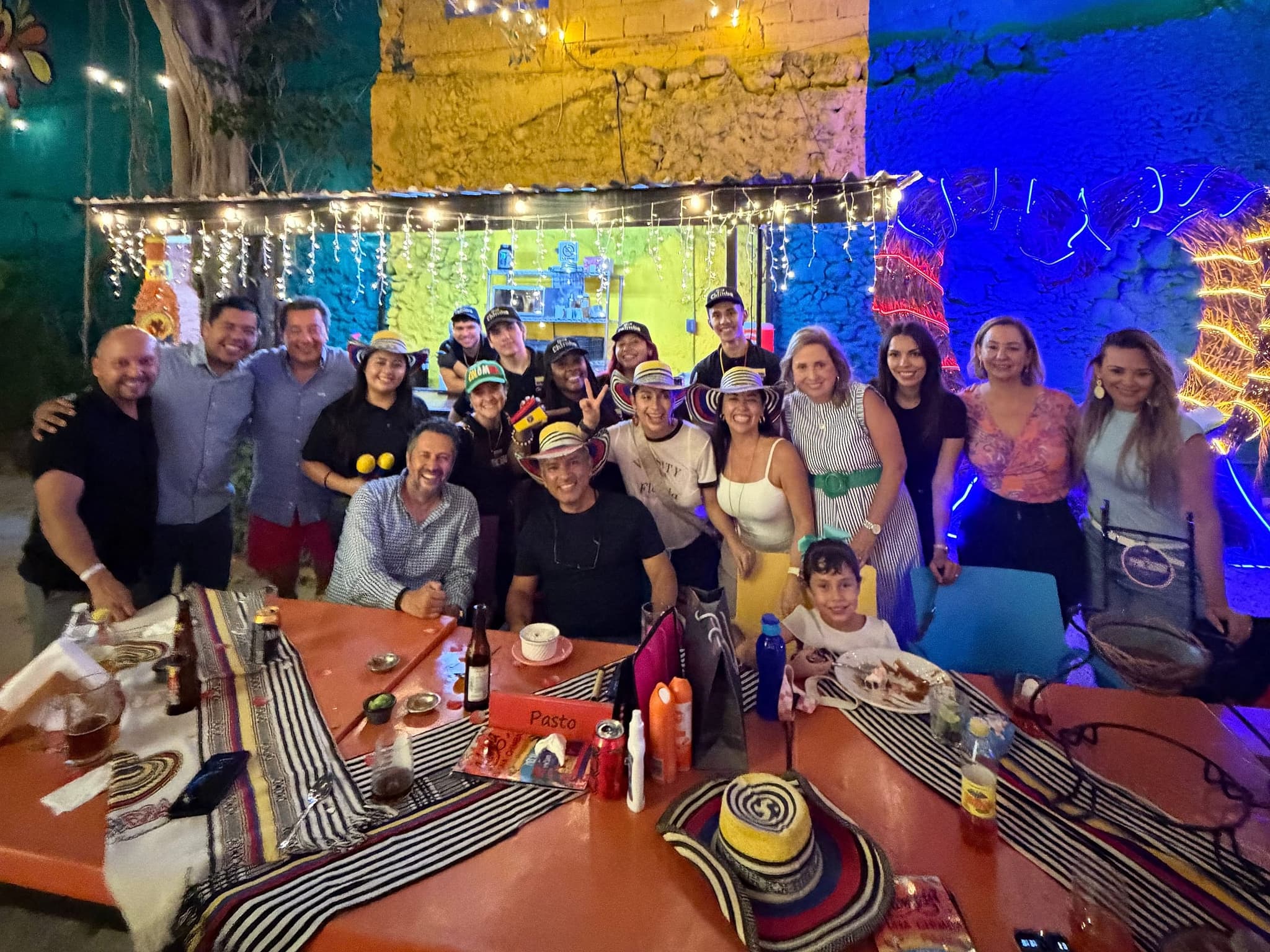 The long table at Parceros full at night: a large group posing in sombreros vueltiaos under the tree with string lights