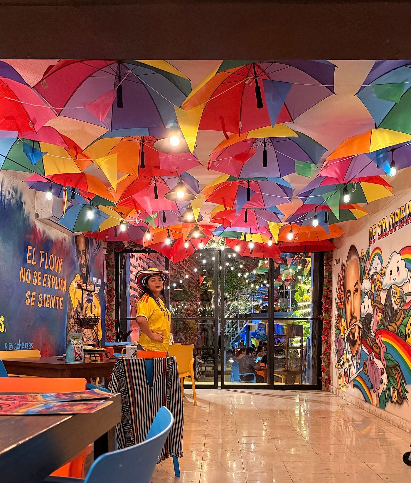 El salón interior de Parceros con el techo cubierto de sombrillas de colores y el mural de «El flow no se explica, se siente»