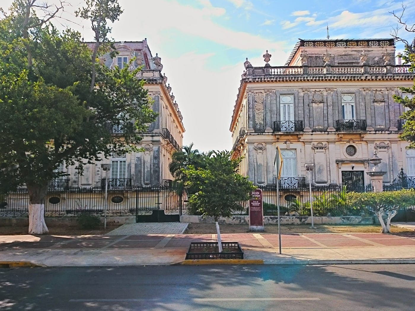 Las dos Casas Gemelas del Paseo de Montejo vistas de frente desde la acera de enfrente, con árboles y una banqueta ancha delante.