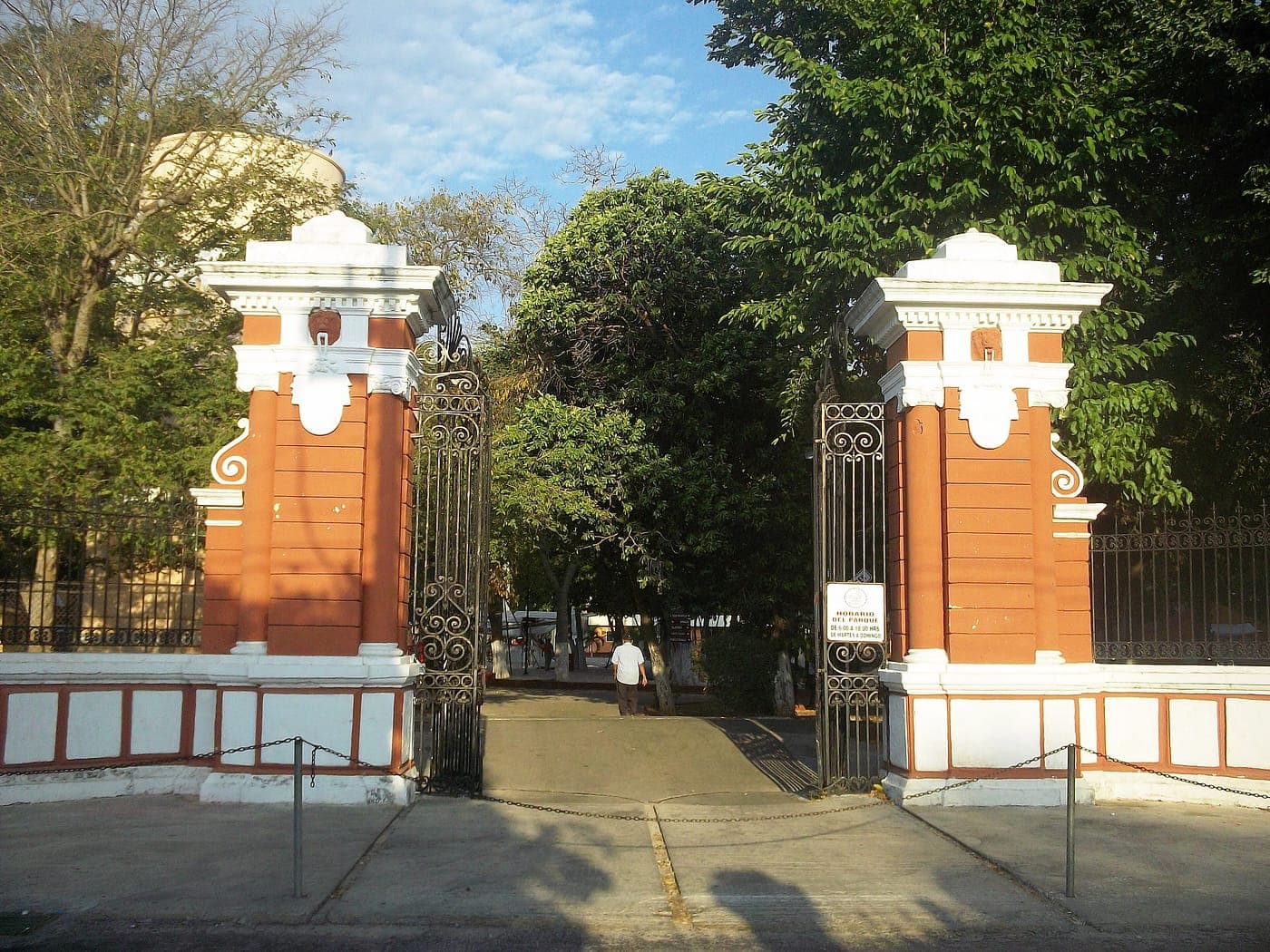 La entrada del Parque Zoológico del Centenario: dos columnas naranjas con rejas de hierro negro, bajo los árboles.