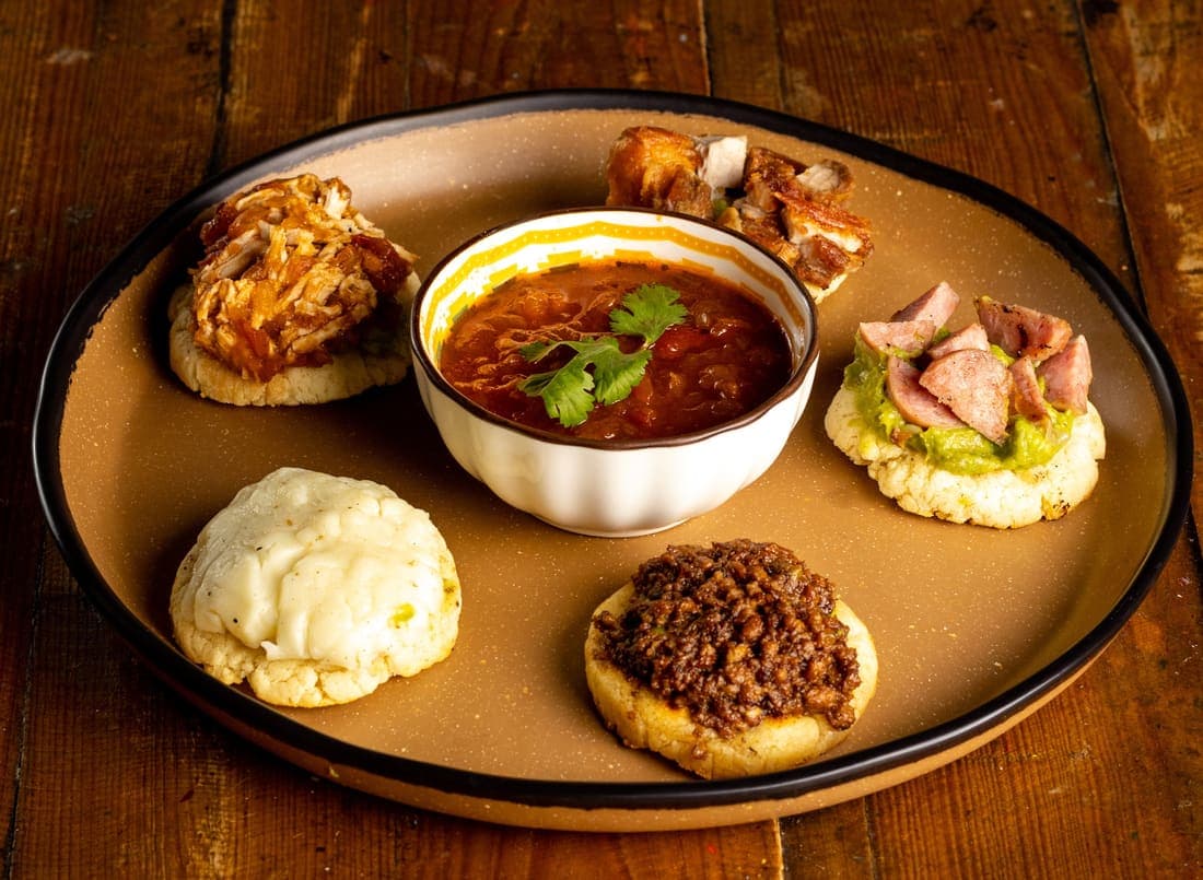 Arepitas Recocheras: Arepitas doraditas sobre base de guacamole, coronadas con pollo, carne molida, chicharrón, chorizo y queso fundido.
