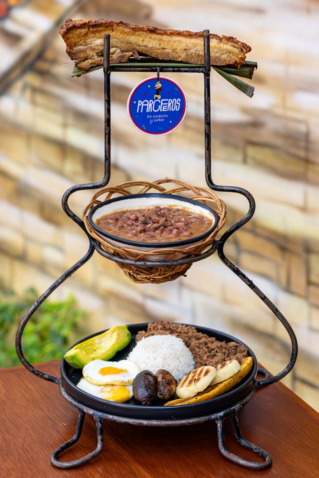 Bandeja Paisa 3 Pisos: chicharrón • chorizo • morcilla • carne • huevo – frijoles • arroz • plátano macho • aguacate • arepa.