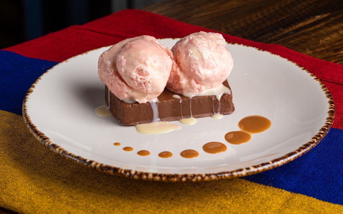 Chocorramo con Helado: El Chocorramo —el ponqué bañado en chocolate de la lonchera colombiana—, servido con bolas de helado cremosas, arequipe y leche condensada.