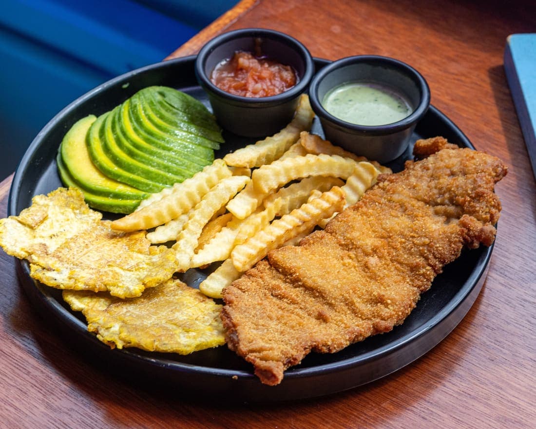 Chuleta Valluna: Chuleta de cerdo empanizada y frita hasta quedar crujiente, servida con papas, patacones y aguacate.