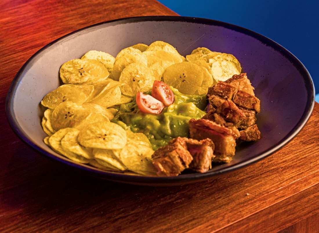 Guacamole con Chicharrón: Guacamole tradicional y sedoso, chicharrón carnoso y chips de plátano: lo crujiente contra lo cremoso en cada bocado.