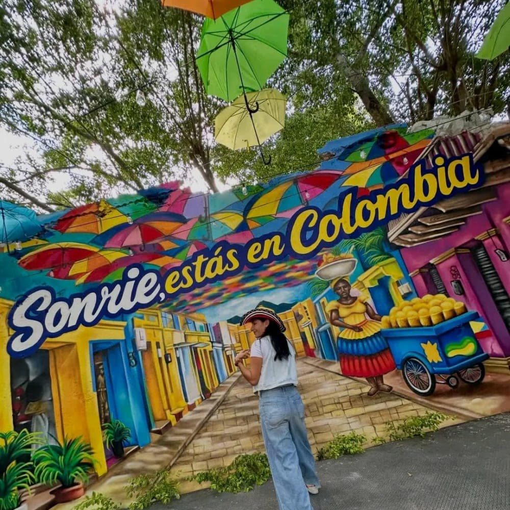 The «Sonríe, estás en Colombia» mural at the entrance to Parceros, under the ceiling of colored umbrellas.